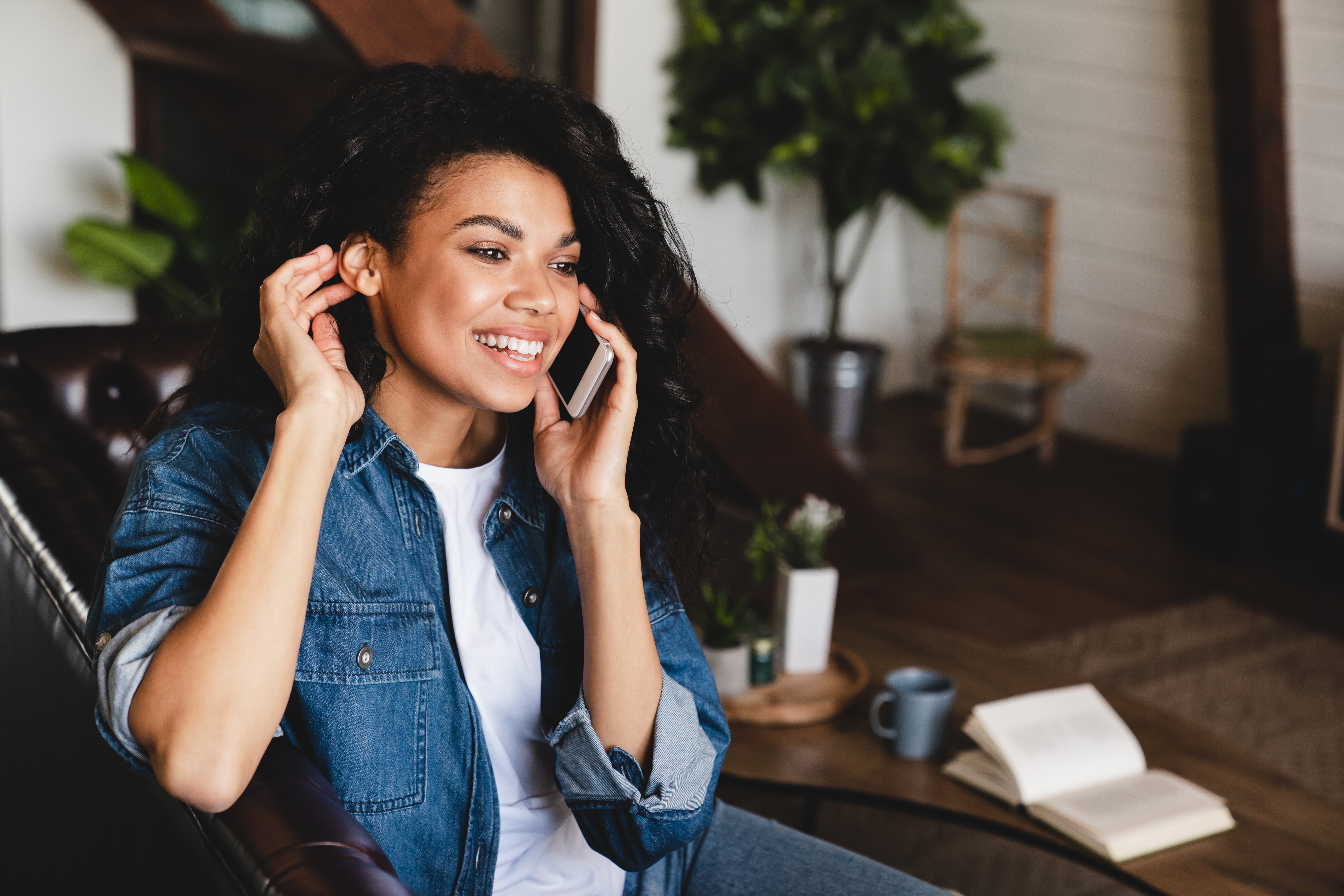 African-american young woman talking on phone in her cosy house. Businesswoman working from home office and using cell phone. Beautiful afro american woman sitting at the desk in a home office and using a smart phone.