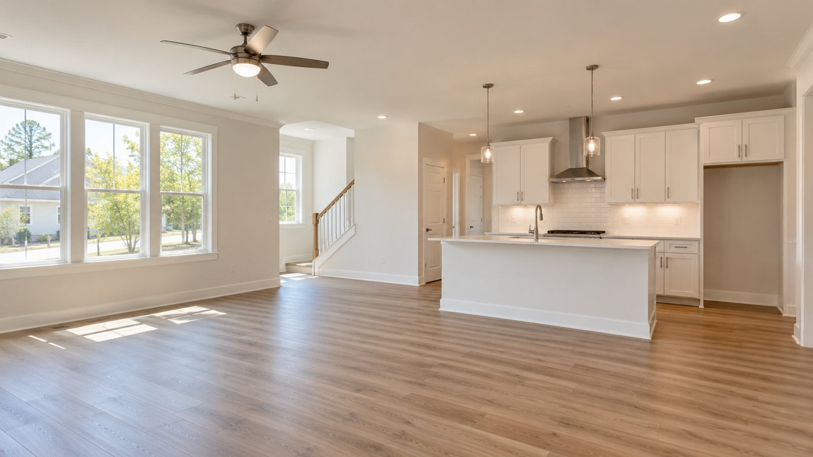 Empty, newly finished open-concept living room and kitchen with white cabinets, island, and wood-look flooring