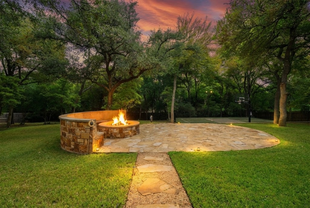 River Place Belton TX backyard with stone fire pit, basketball court, and mature oak trees at twilight