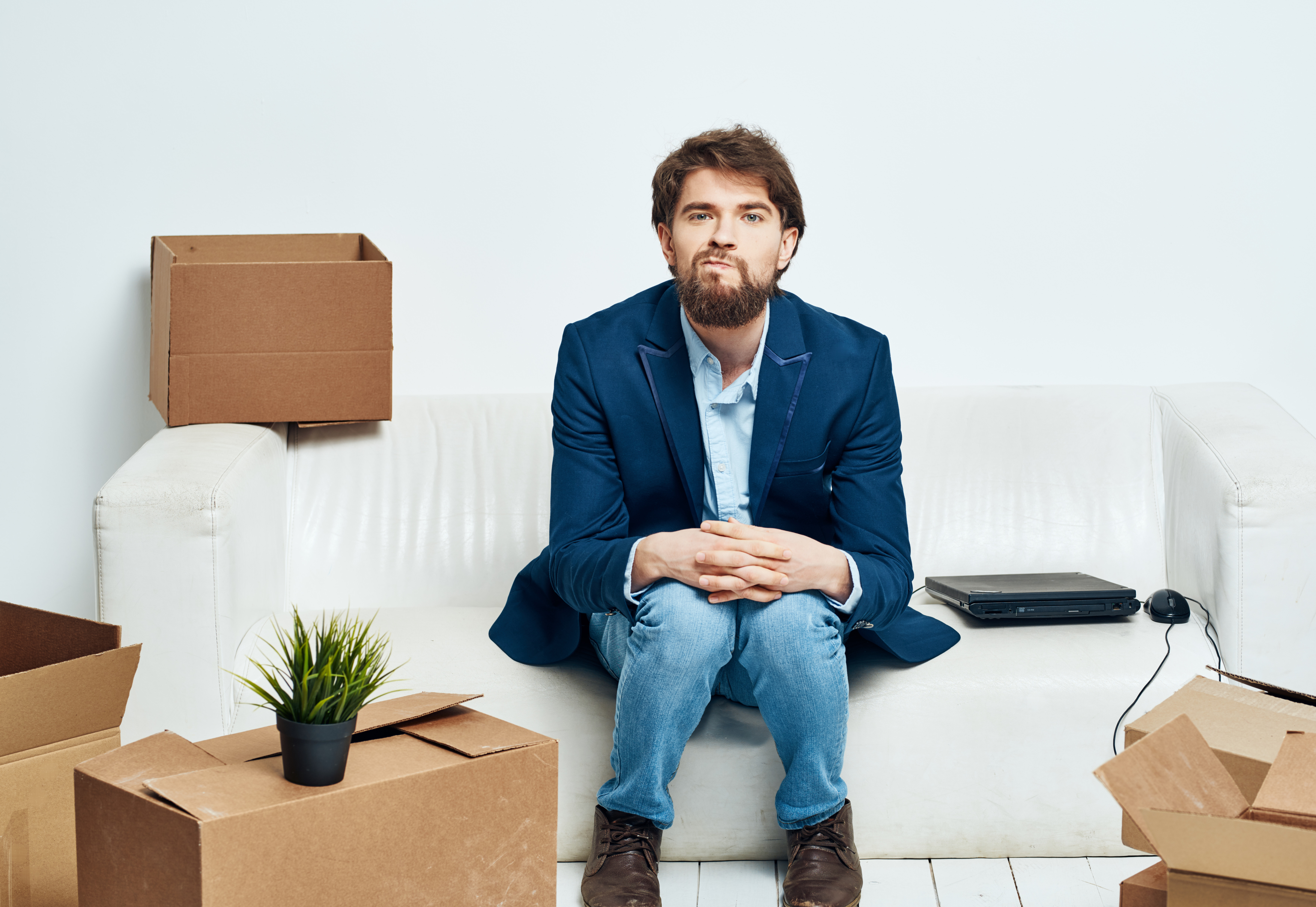 A man sits on the couch next to boxes unpacking a new moving location