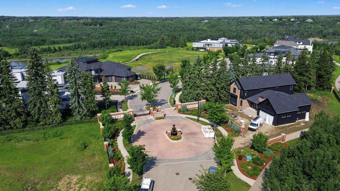 Landscaped entry circle inside The Banks with mature spruce and a completed contemporary estate home.