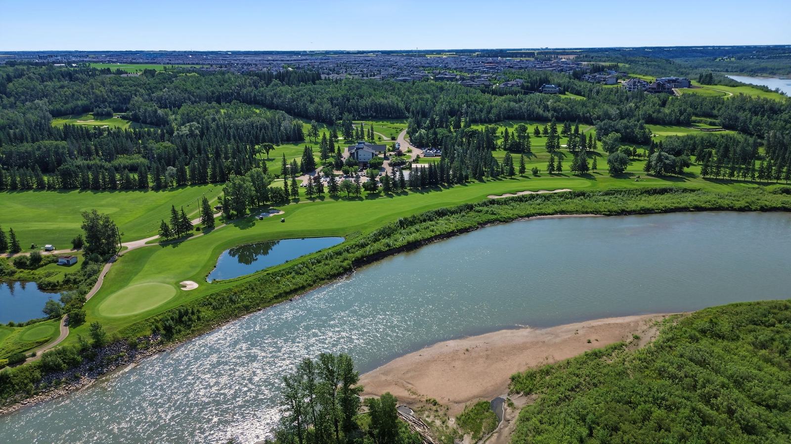 A wide bend in the North Saskatchewan River with fairways and treed slopes along the bank.