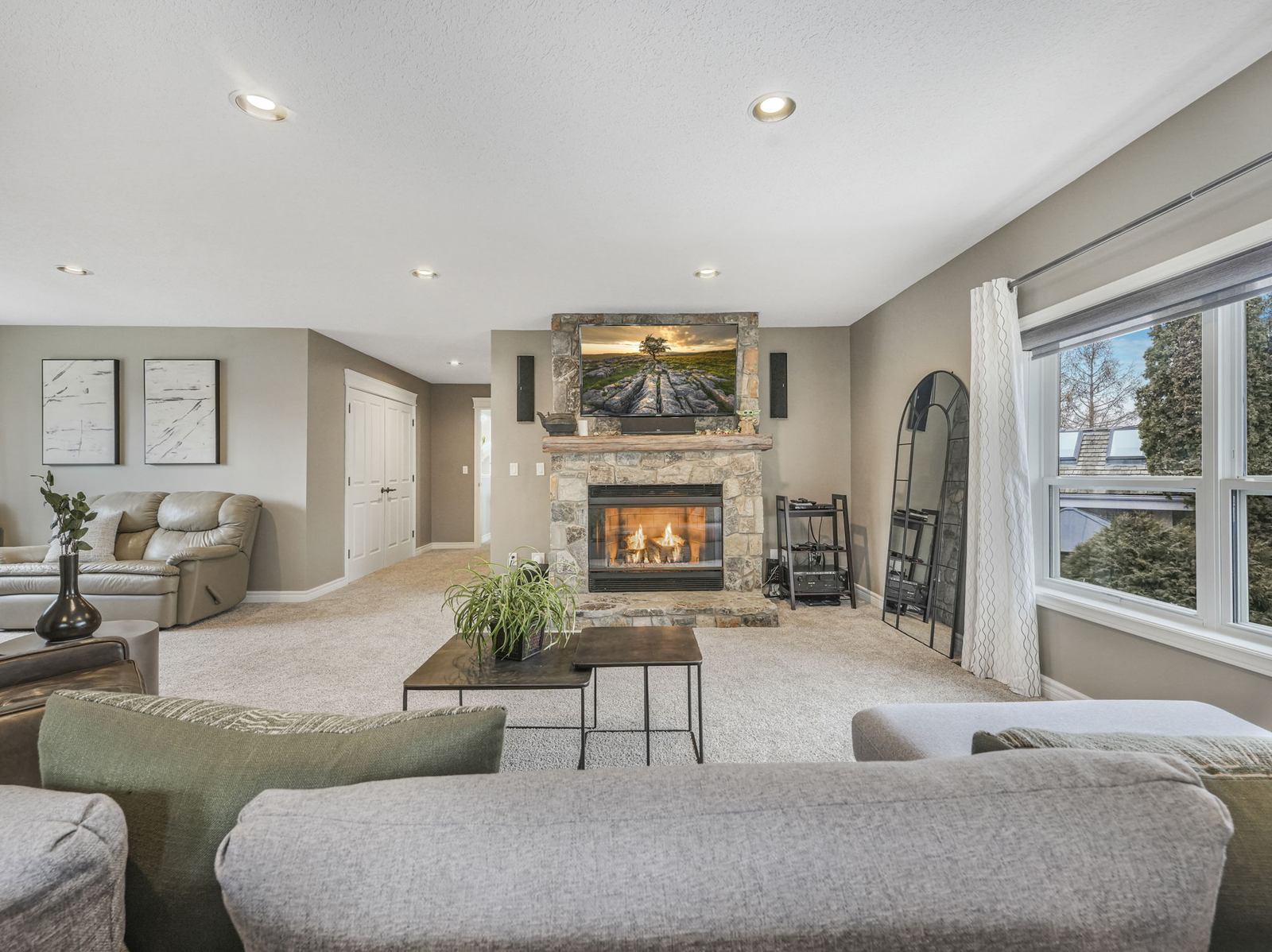 The upper bonus room, a large carpeted space with the second gas fireplace set into stone under a raised mantle.