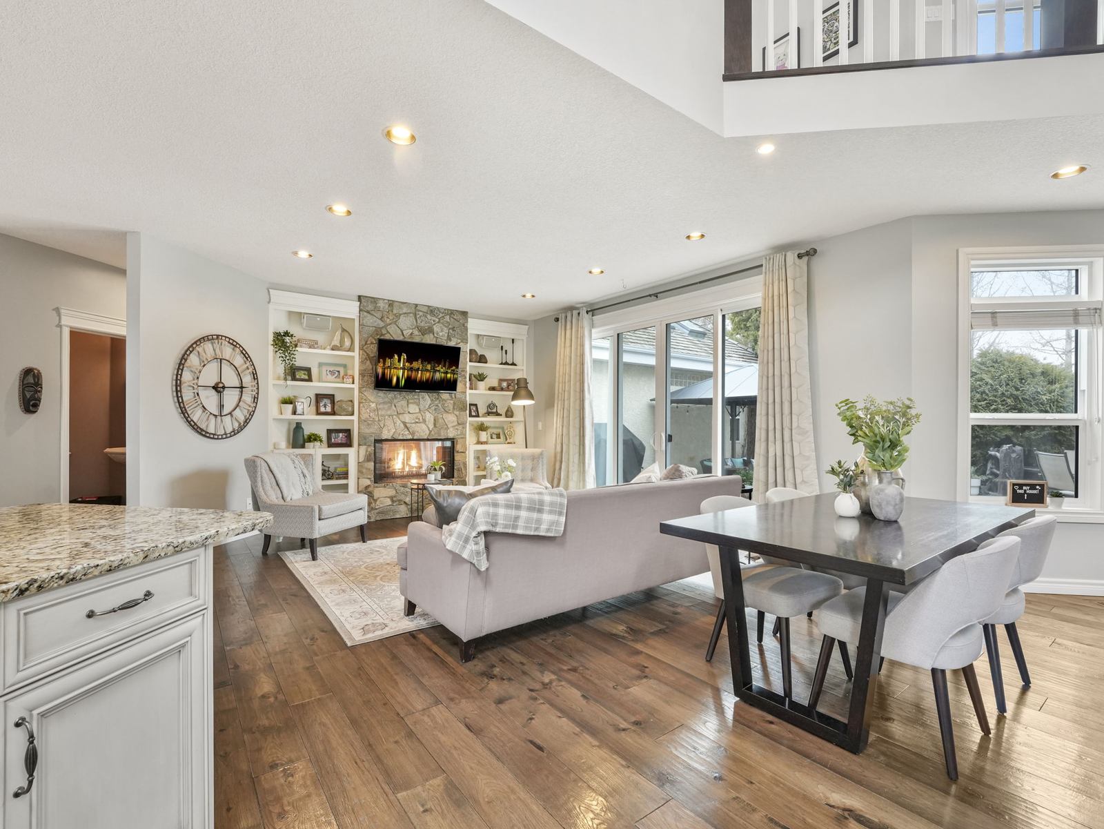 The dining area open to the family room, with engineered hardwood throughout and the stone fireplace beyond.