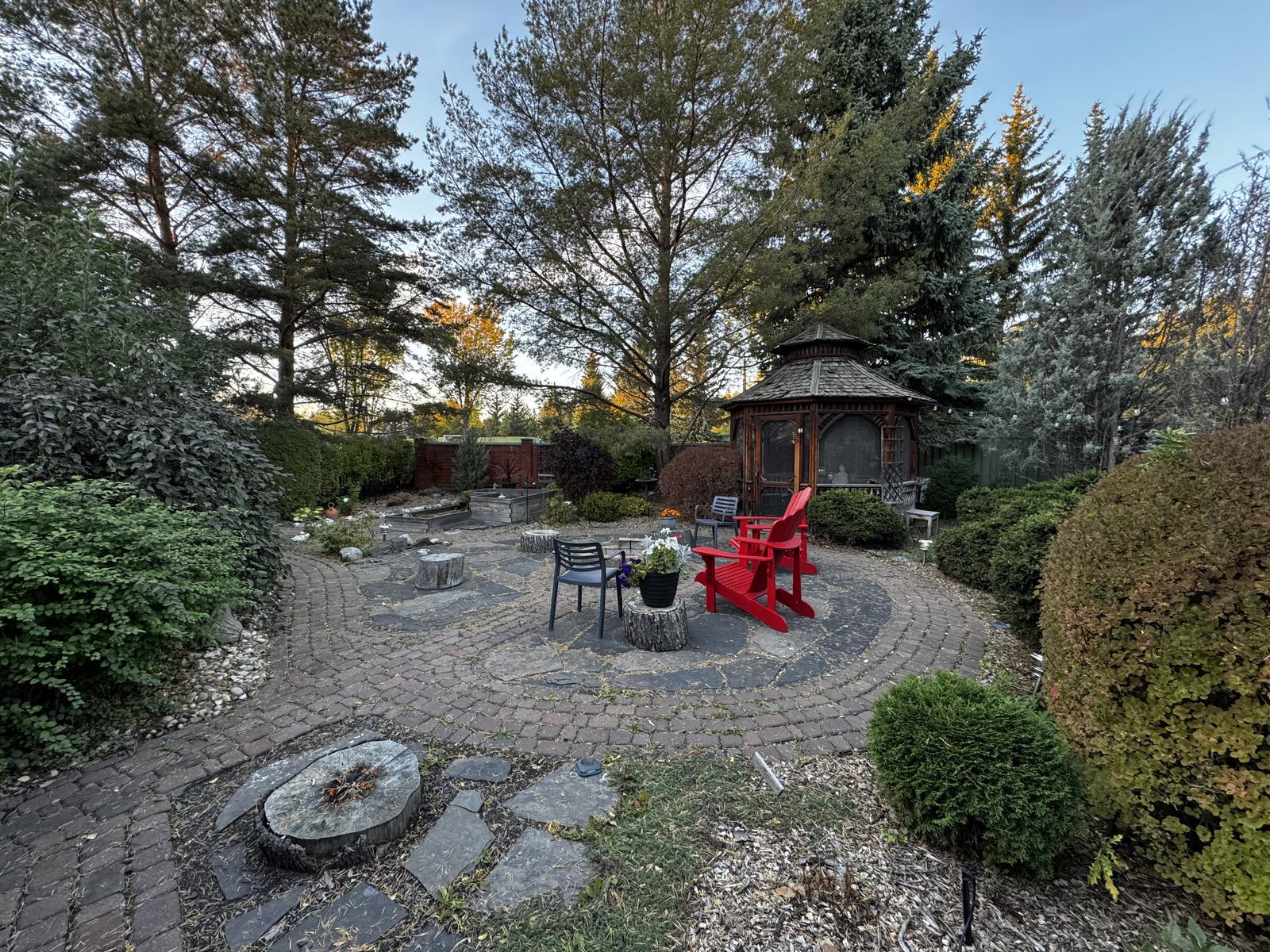 The flagstone fire pit terrace in daylight, laid in circles with red chairs and the gazebo behind.