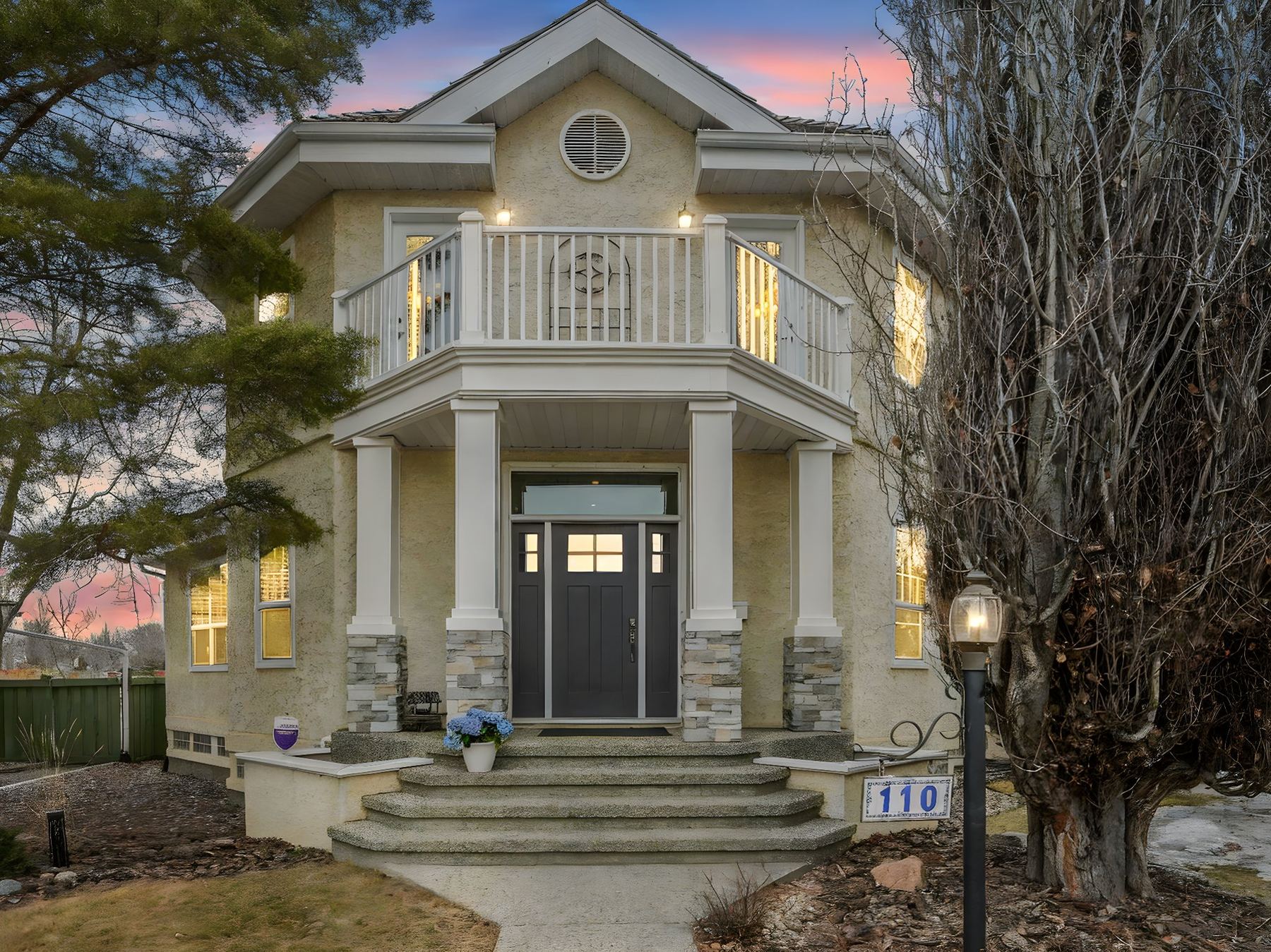 The front elevation of 110 Weaver Drive at dusk, stucco and stone with a covered portico and lit windows.