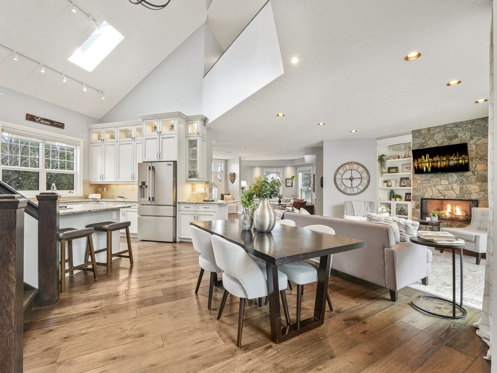 The kitchen under a vaulted ceiling with skylights, granite counters, white cabinetry and stainless appliances.