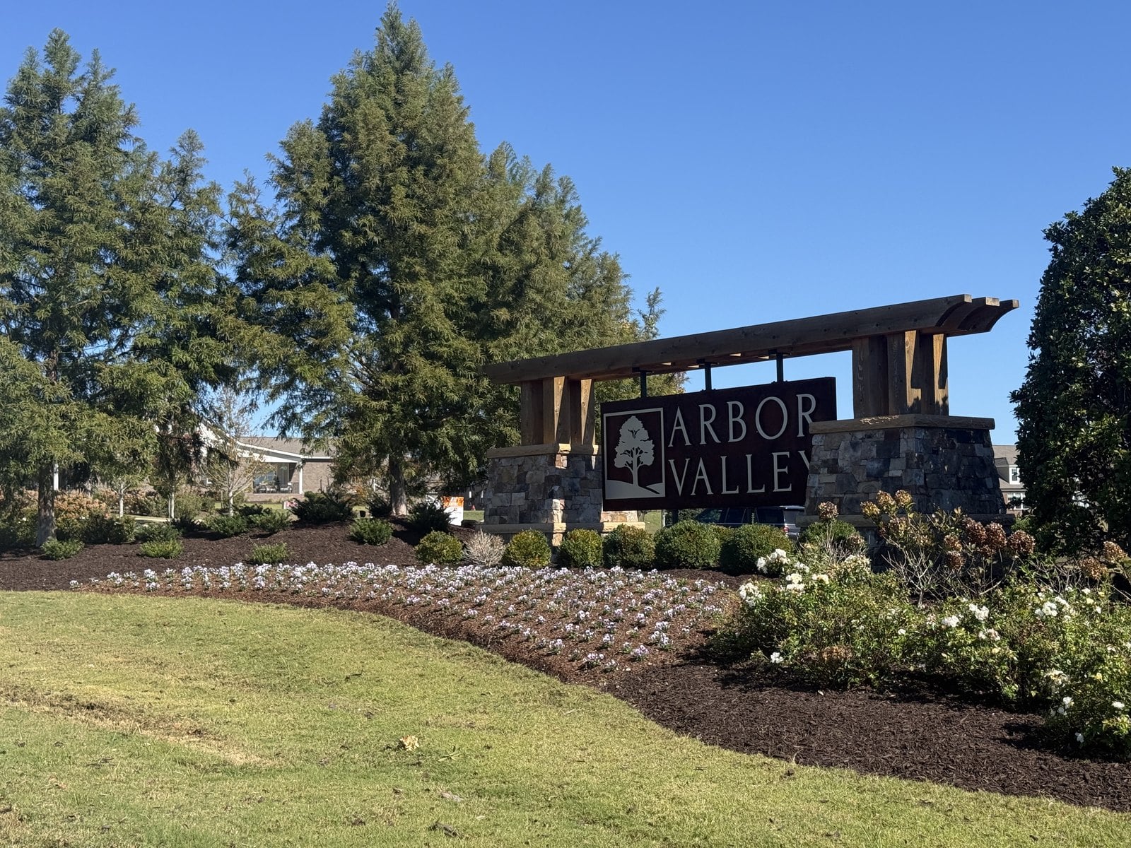 Arbor Valley stone and timber entrance sign with evergreens and a flower bed in Spring Hill, TN.