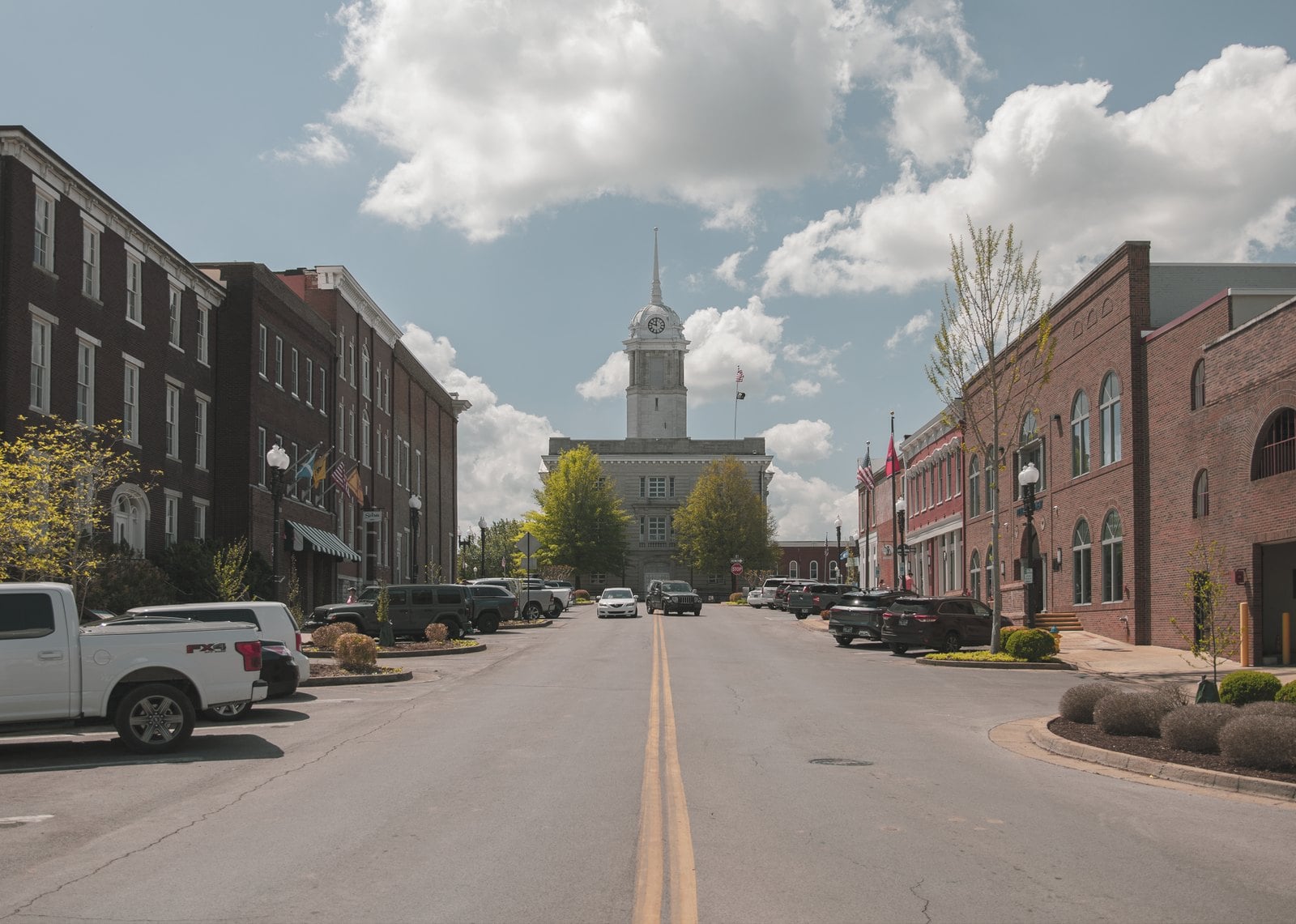 Downtown street in Columbia, TN, lined with brick buildings and parked cars, leading to the Maury County Courthouse and its clock tower