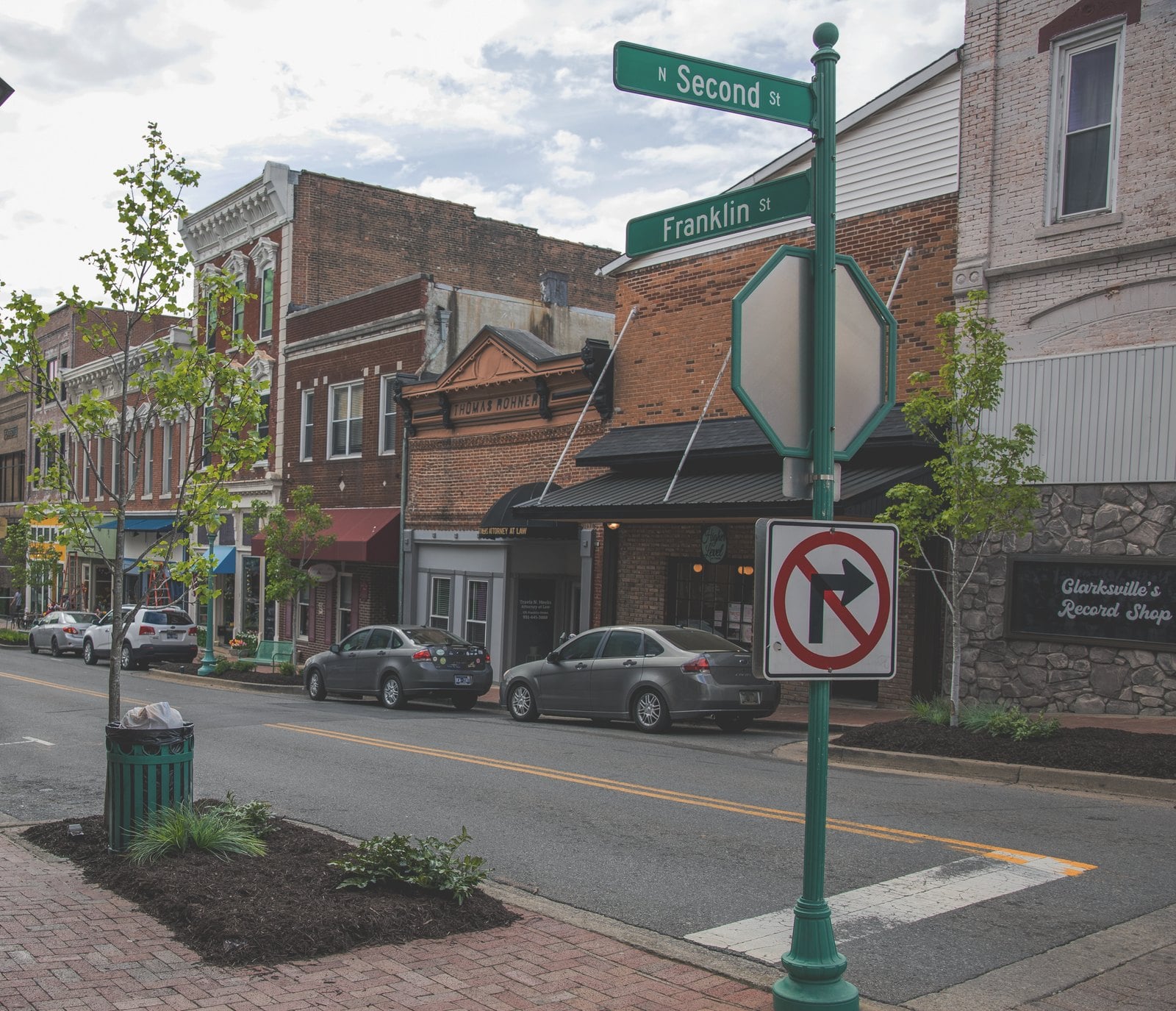 Brick storefronts along Franklin Street at North Second Street in downtown Clarksville, with green street signs and young trees.