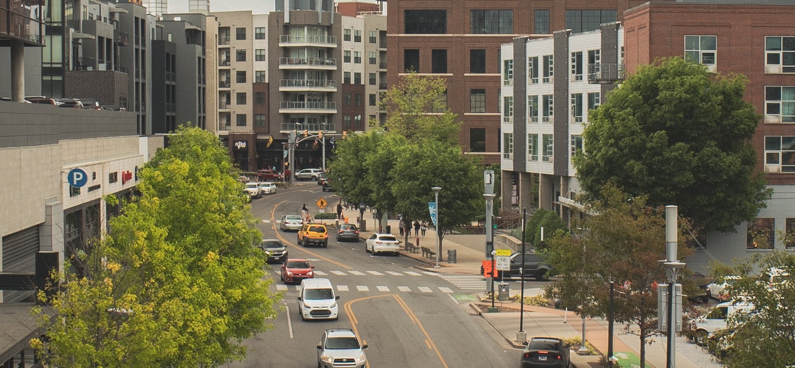 A two-lane street through the Gulch in downtown Nashville with cars, street trees, and condo and office buildings on both sides