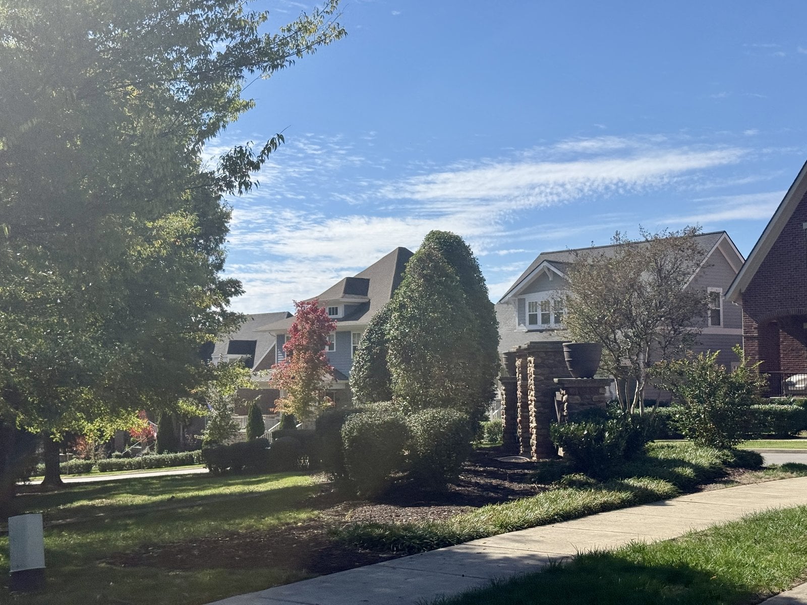 Two-story homes behind clipped shrubs, stone pillars and a sidewalk in Lockwood Glen, Franklin.