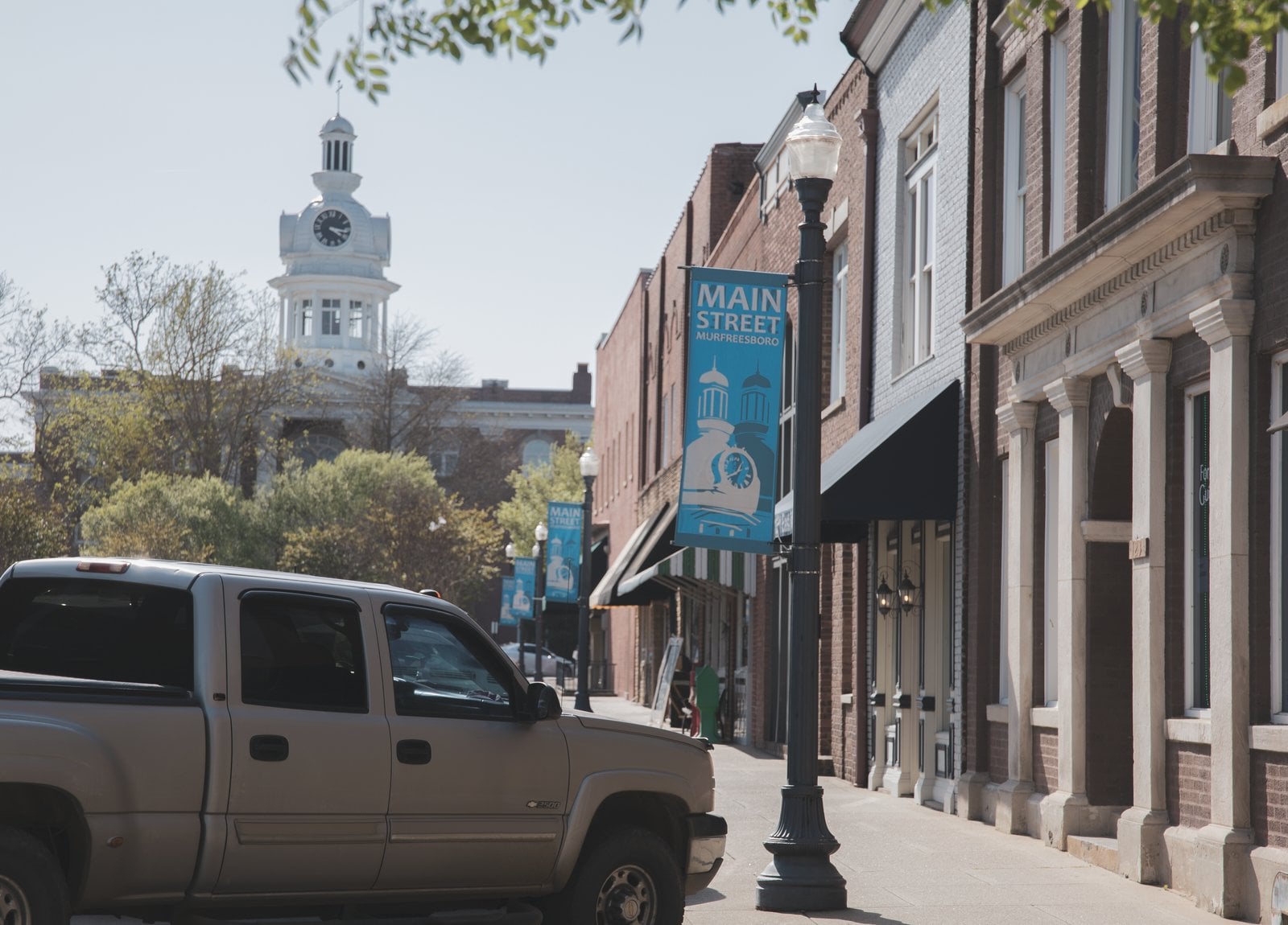Main Street Murfreesboro banner on a lamppost beside brick storefronts, with the white courthouse cupola behind the trees at the end of the block