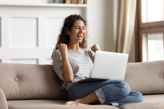 Woman sit on sofa put pc on lap clenched fists scream with joy while read great news on laptop. Gambler celebrate online auction bet victory.