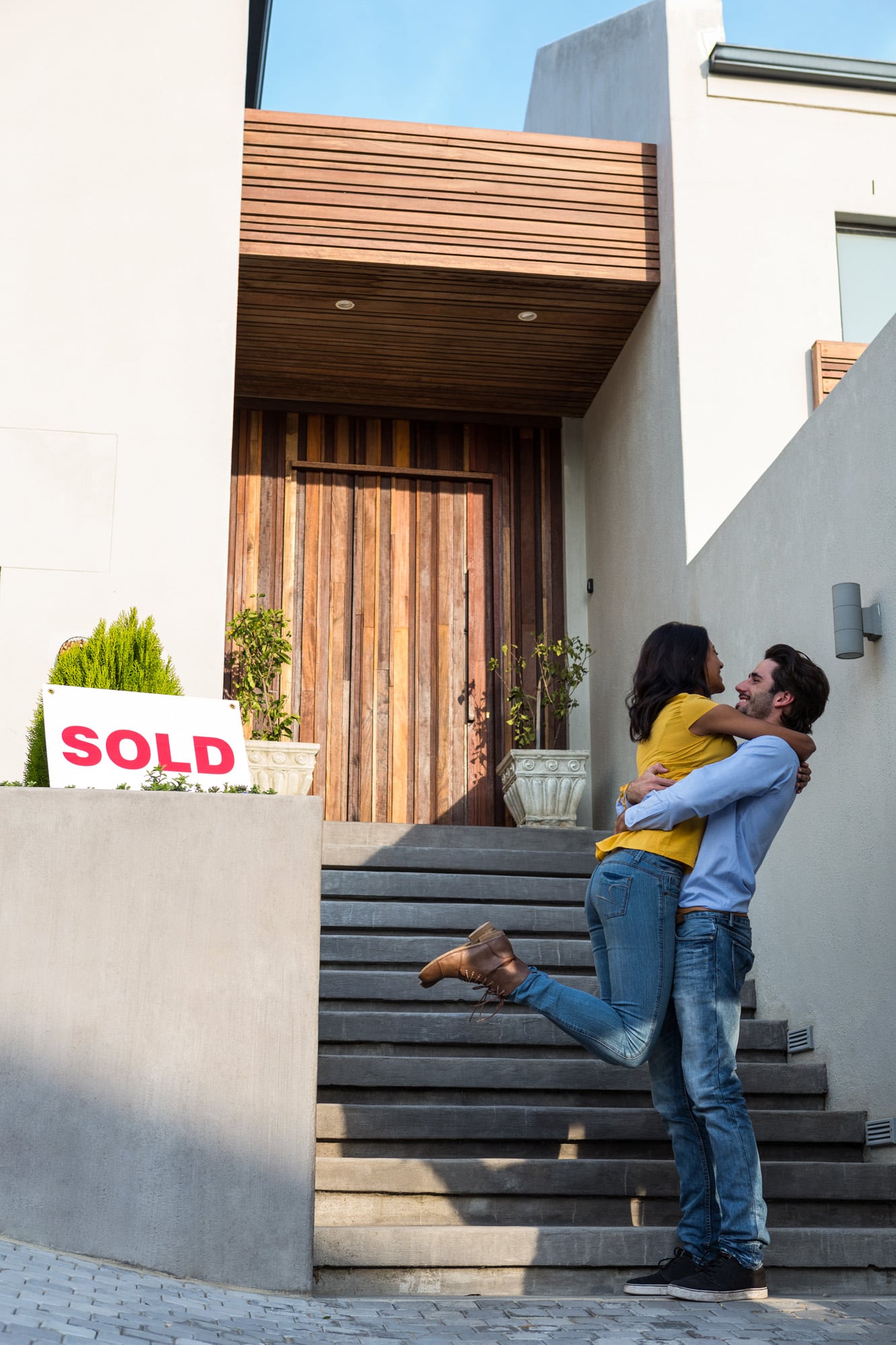 Happy,Hispanic,Couple,Hugging,In,Front,Of,New,House