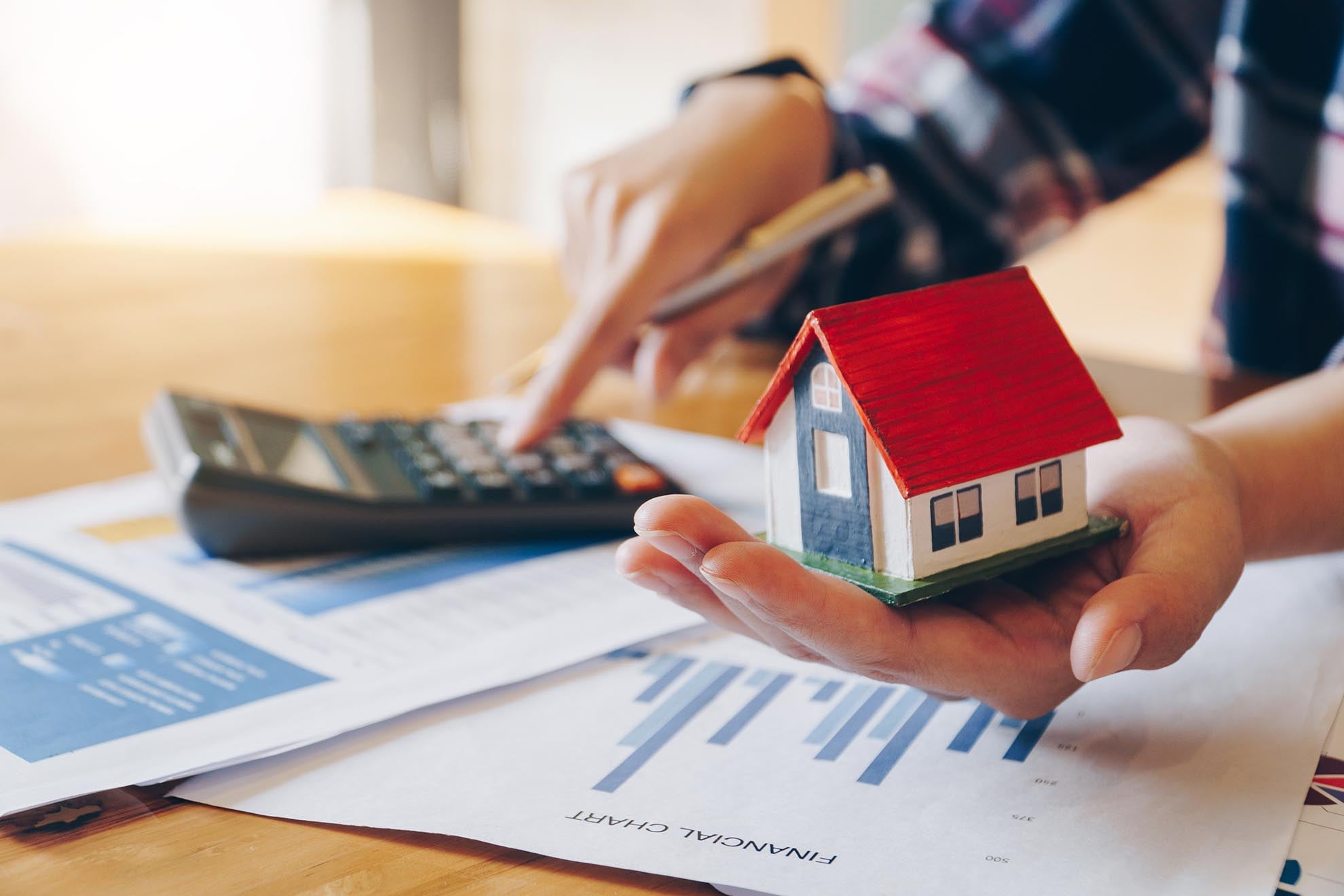 Woman holding house model in hand and calculating financial char