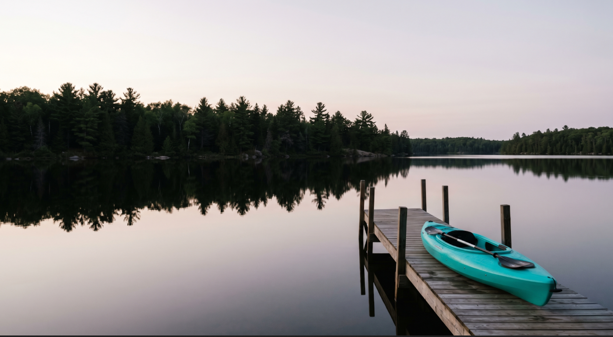 Teal kayak on Eastern Ontario waterfront dock at dusk, mirror reflection.