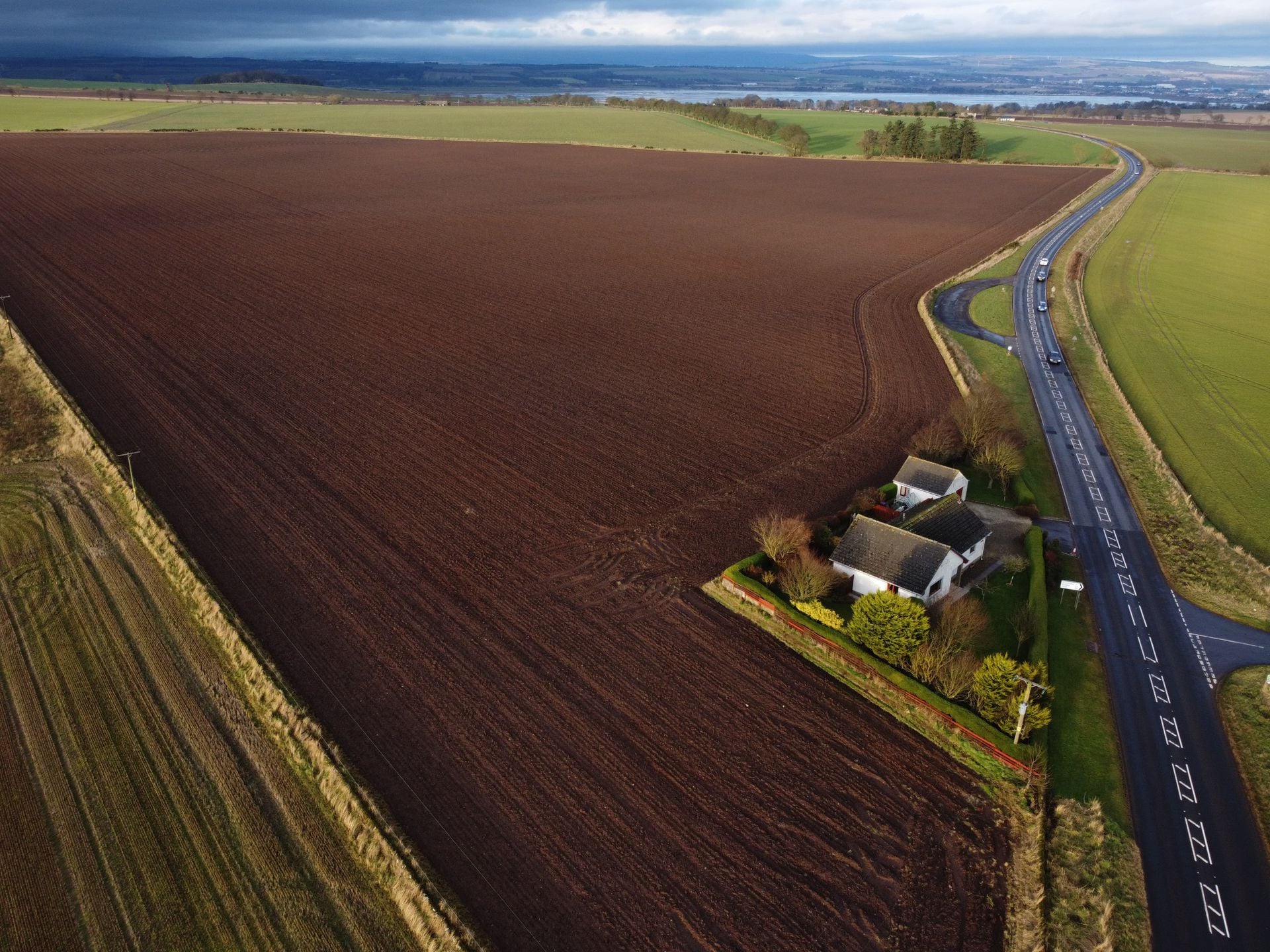 Aerial view of open farmland beside a country road with a single home on the edge of the field