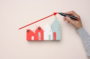 A miniature wooden house and a woman's hand draws a graph with growing indicators.