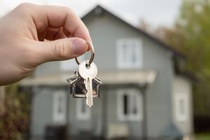 Hand holding key in front of new house