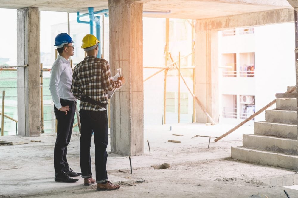 Two contractors in hard hats reviewing an unfinished interior construction project in a home under renovation