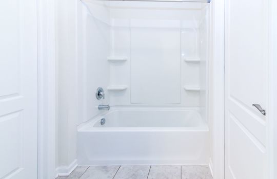 image shows a white, standard-sized bathtub with an integrated shower unit, likely part of a pre-fabricated or modular bathroom system often found in townhomes or apartments