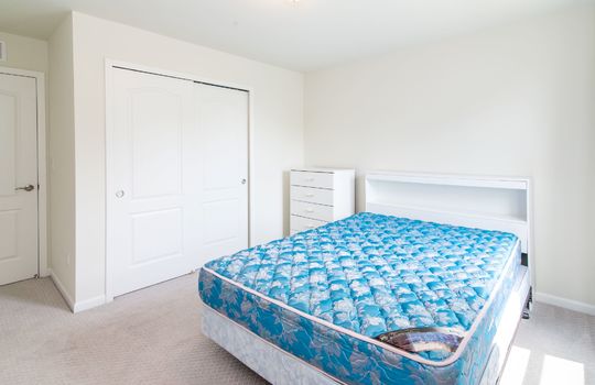 A bedroom with a bed, a white dresser, and a closet with sliding doors.