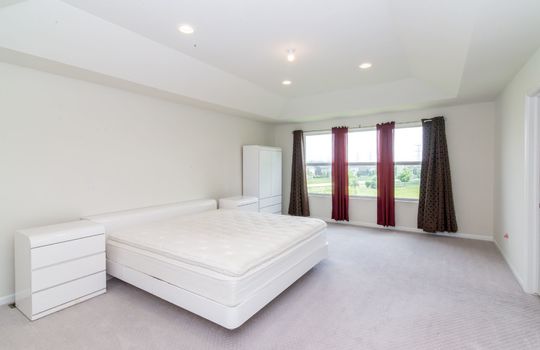 A bedroom with a white bed, white nightstands, a white armoire, and red curtains.