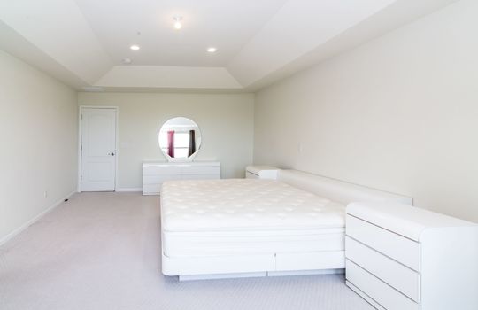 A bedroom with a white bed, white nightstands, a white dresser, and a mirror