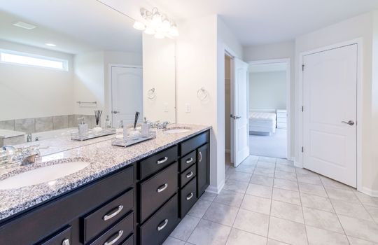 This is an image of a bathroom. It shows a double vanity with a granite countertop, a large mirror, two sinks, a shower stall, and a white door