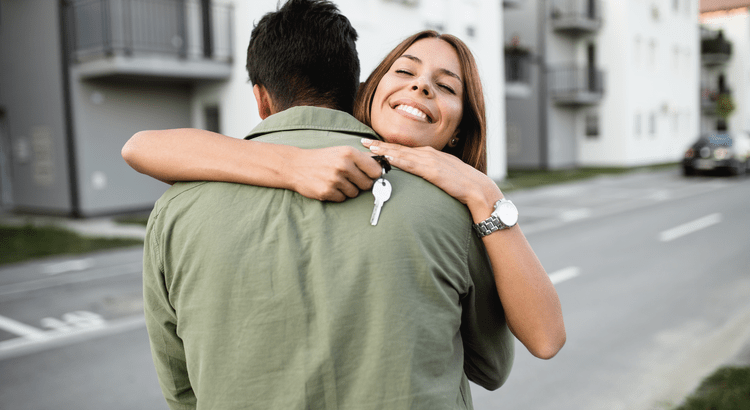 image shows a woman embracing a man from behind, holding a house key in her hand