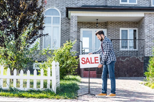 image shows a "For Sale" sign in front of a house, indicating that the property is on the market