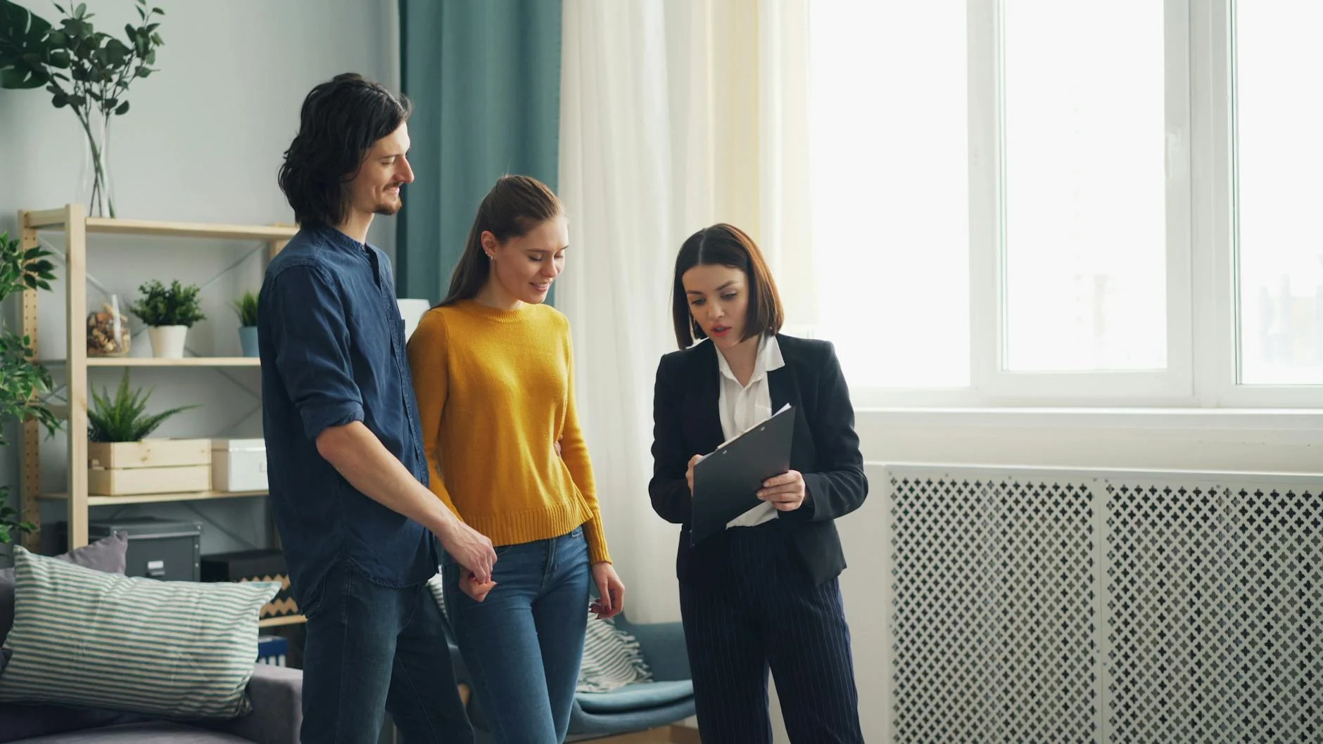 A young couple discusses home buying options with a real estate agent inside a well-lit modern room, symbolizing the excitement and decision-making process of first-time homebuyers.