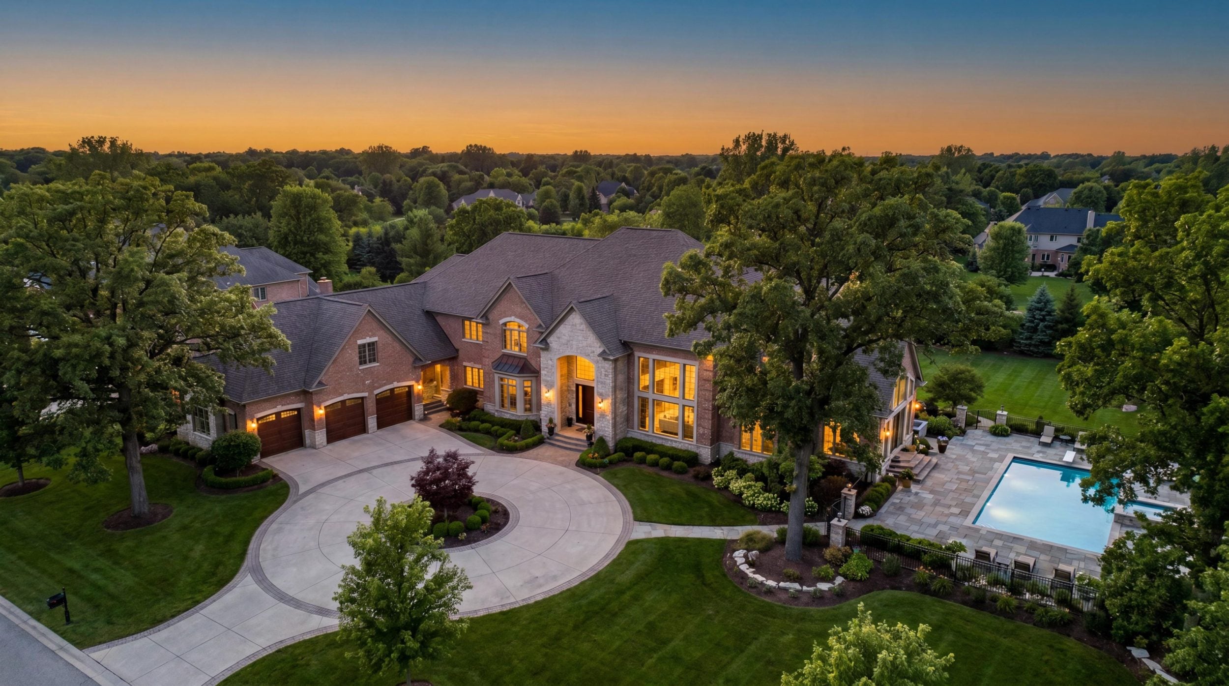 Luxury estate home for sale in Farmington Hills Michigan at golden hour — custom brick and stone architecture with circular driveway pool and professional landscaping — aerial drone photography — Tom Gilliam RE/MAX Classic top luxury Realtor Farmington Hills Oakland County Michigan — Homes2MoveYou.com 248-790-5594