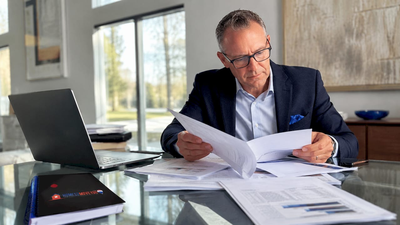 Realtor in Farmington Hills reviewing appraisal documents and paperwork at a desk with a laptop