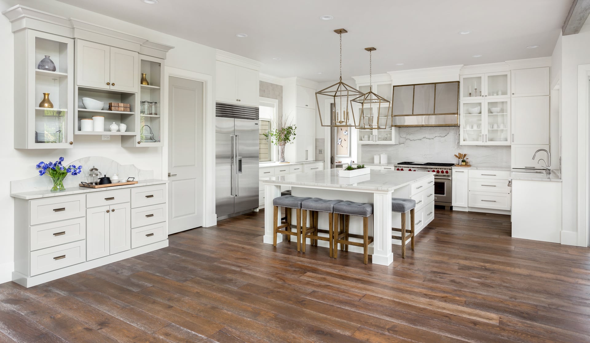 Beautiful-kitchen-interior-in-new-luxury-home,-with-white-cabinets-and-woodwork,-pendant-lights,-stainless-steel-appliances,-and-large-kitchen-island.-Features-stainless-steel-range-hood.