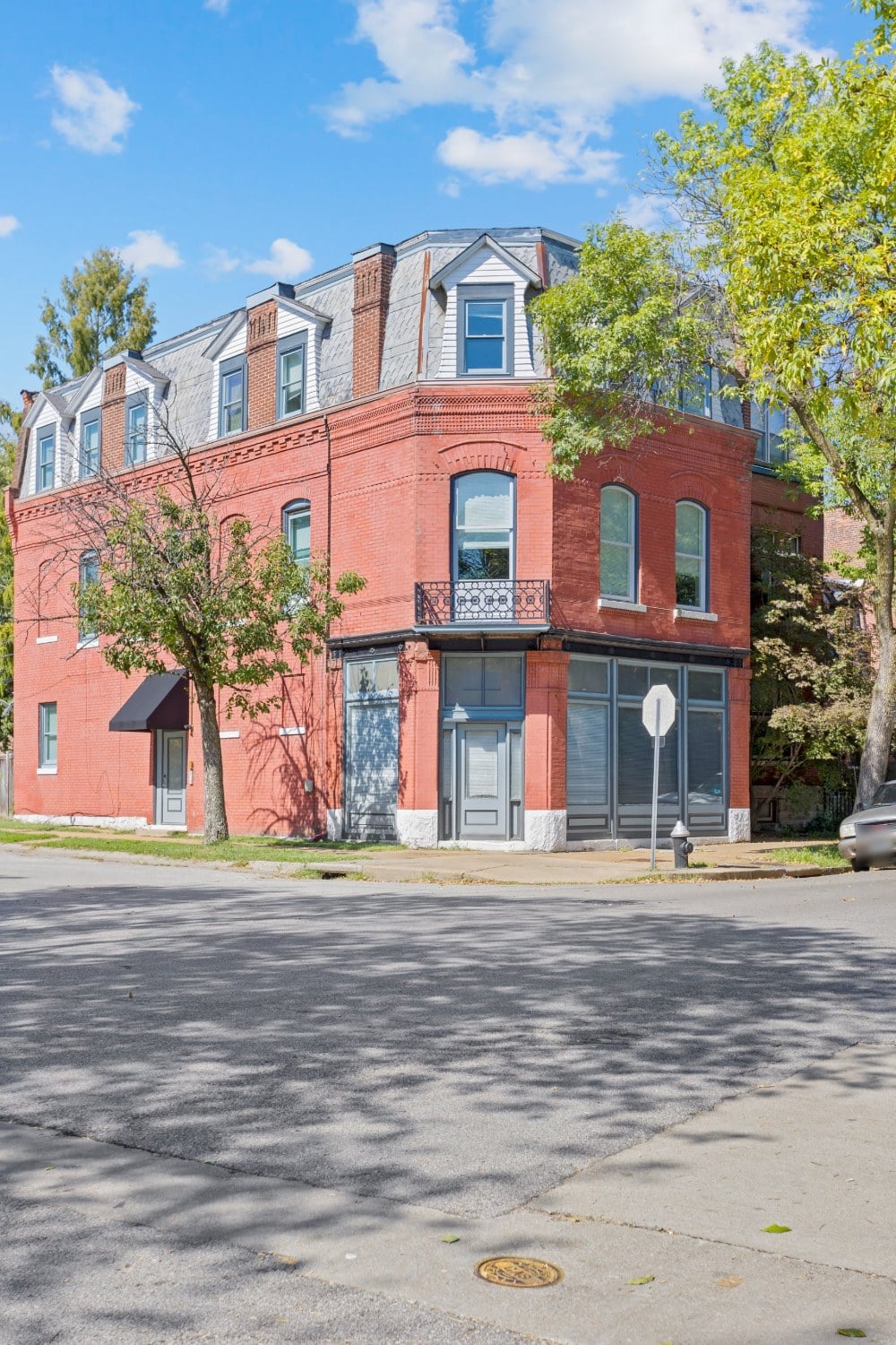 Full view of a historic red brick corner building in St. Louis with a slate mansard roof, dormers and a corner storefront