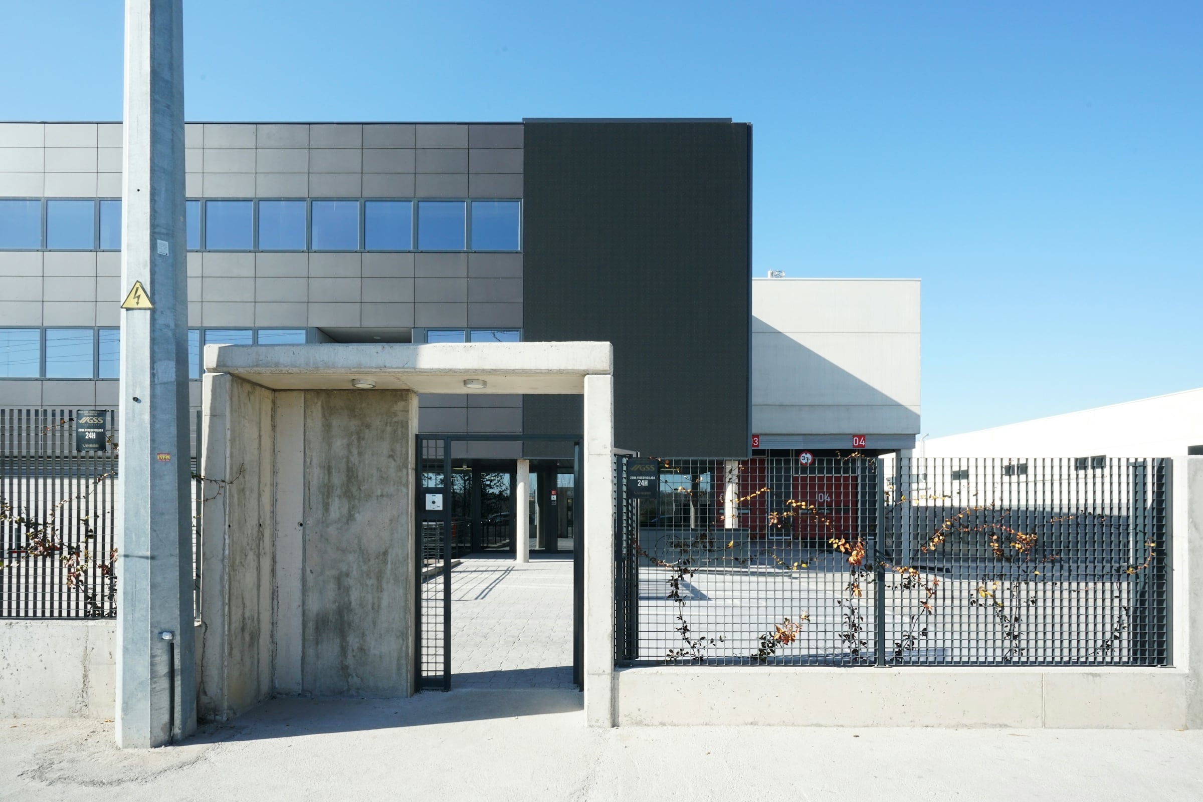 Low-rise dark-clad data center building behind a secured perimeter fence and gated concrete entrance
