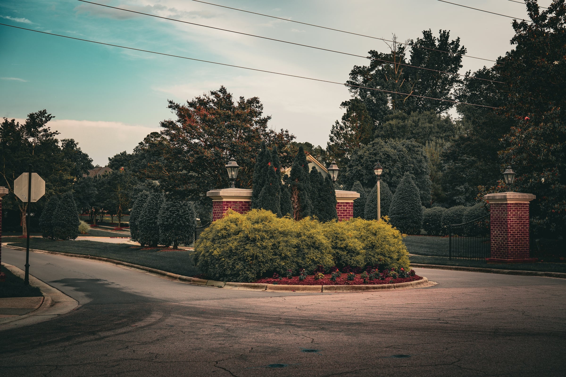 Neighborhood entrance with brick pillars, lamp posts and a landscaped median on a curving street