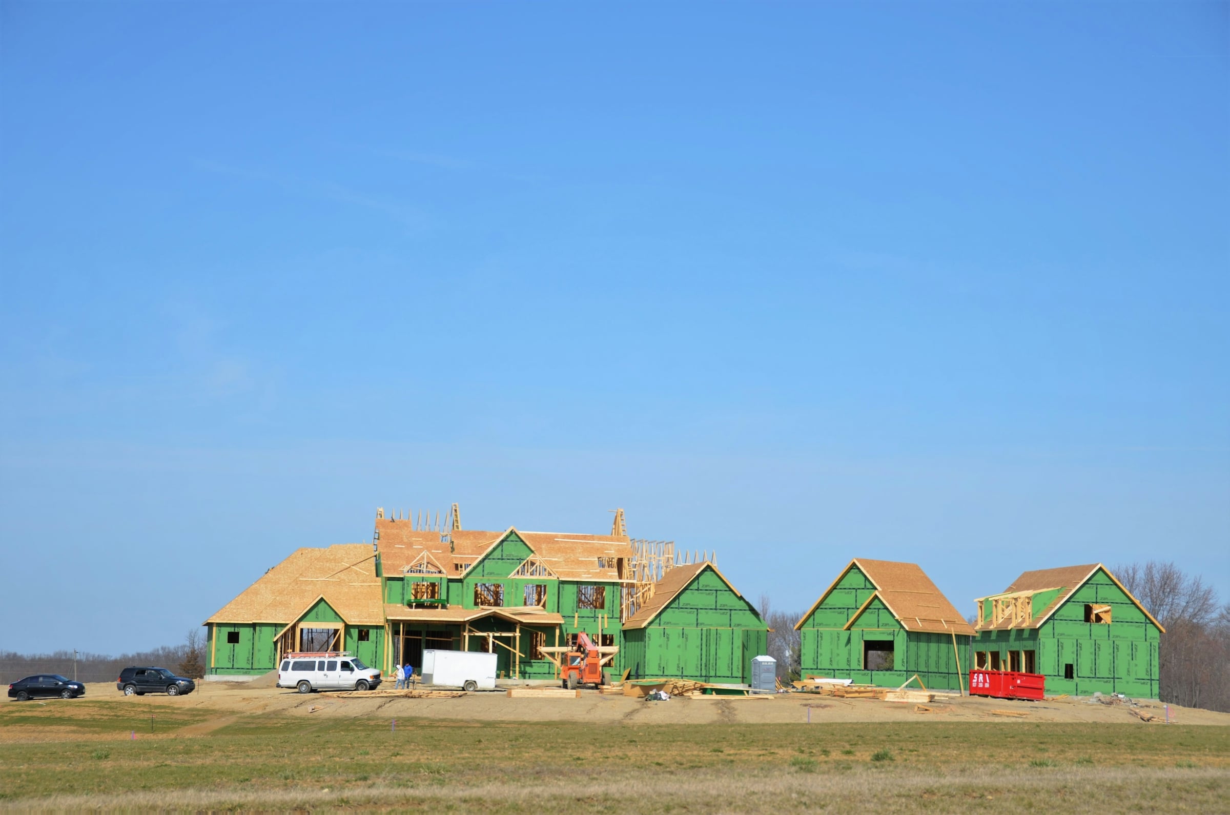 Row of wood-framed houses under construction with green sheathing on bare dirt lots