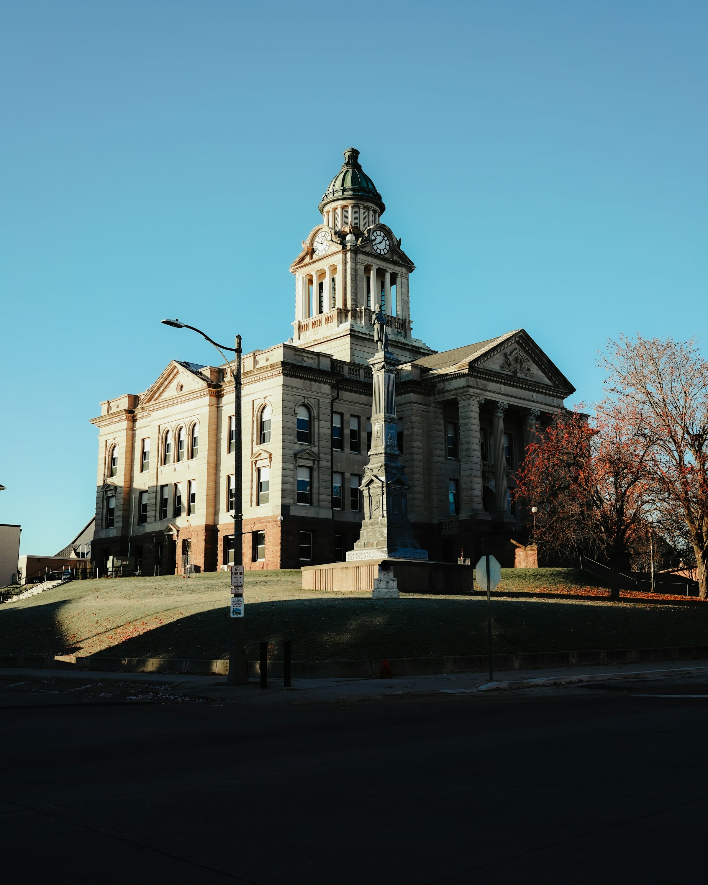 County courthouse exterior with a clock tower, columned portico and a stone monument on the lawn
