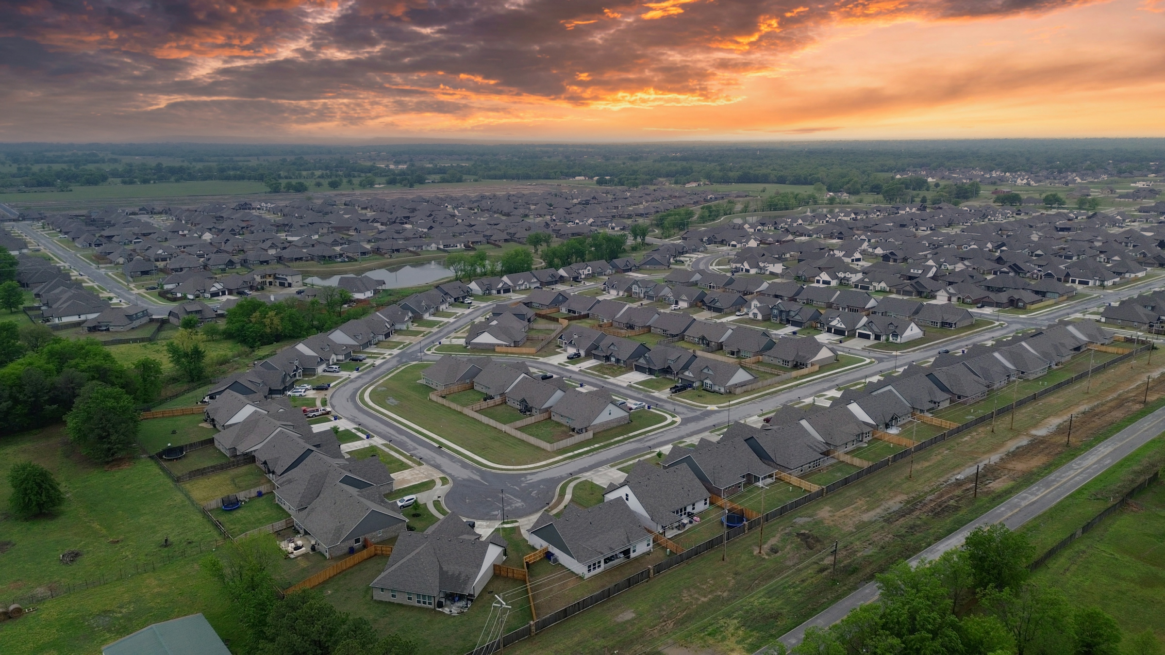 Aerial view at sunset of a new residential subdivision with curving streets and undeveloped land at the edges
