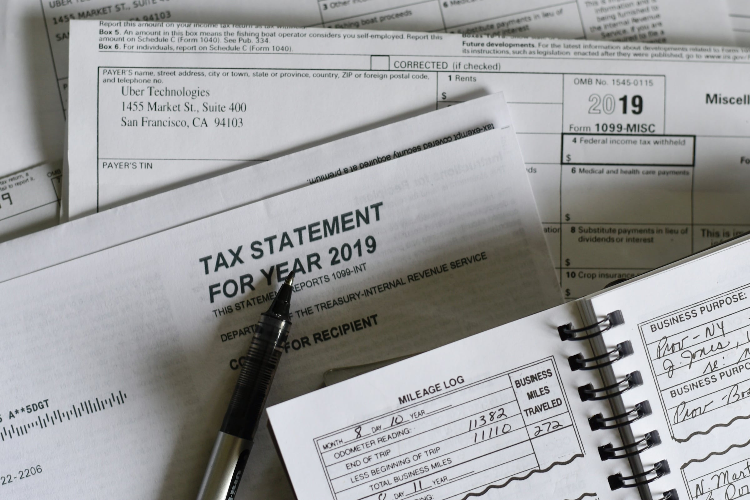 Printed tax statement and 1099 forms spread on a desk beside a mileage log book and pen