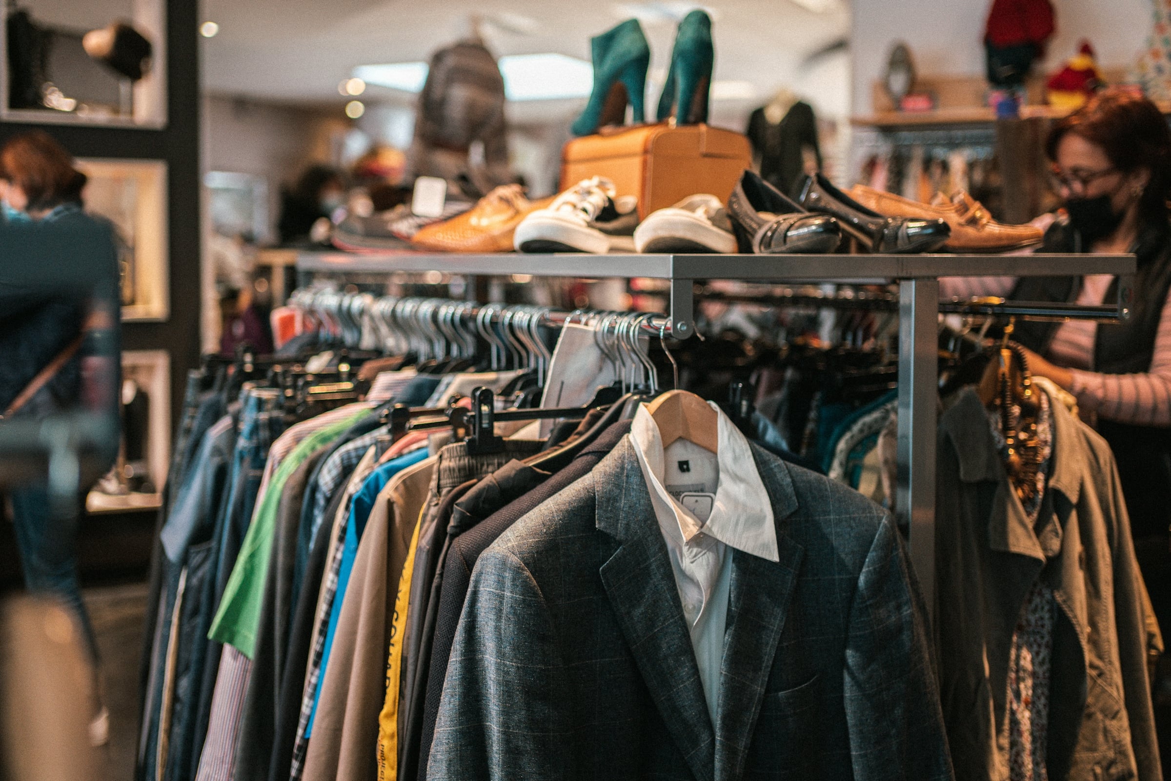 Secondhand store interior with a packed rack of coats and blazers and used shoes on a shelf above