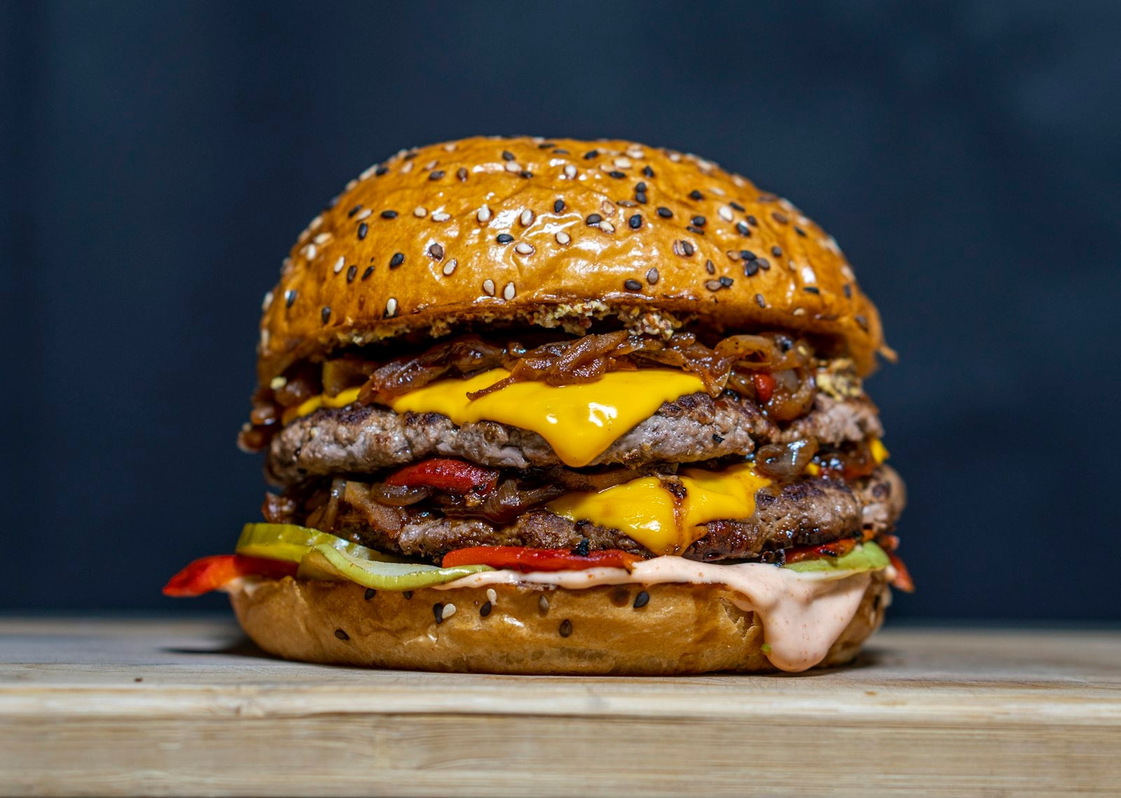Close-up of a double-patty smashed cheeseburger with melted cheese, pickles and sauce on a wooden surface.