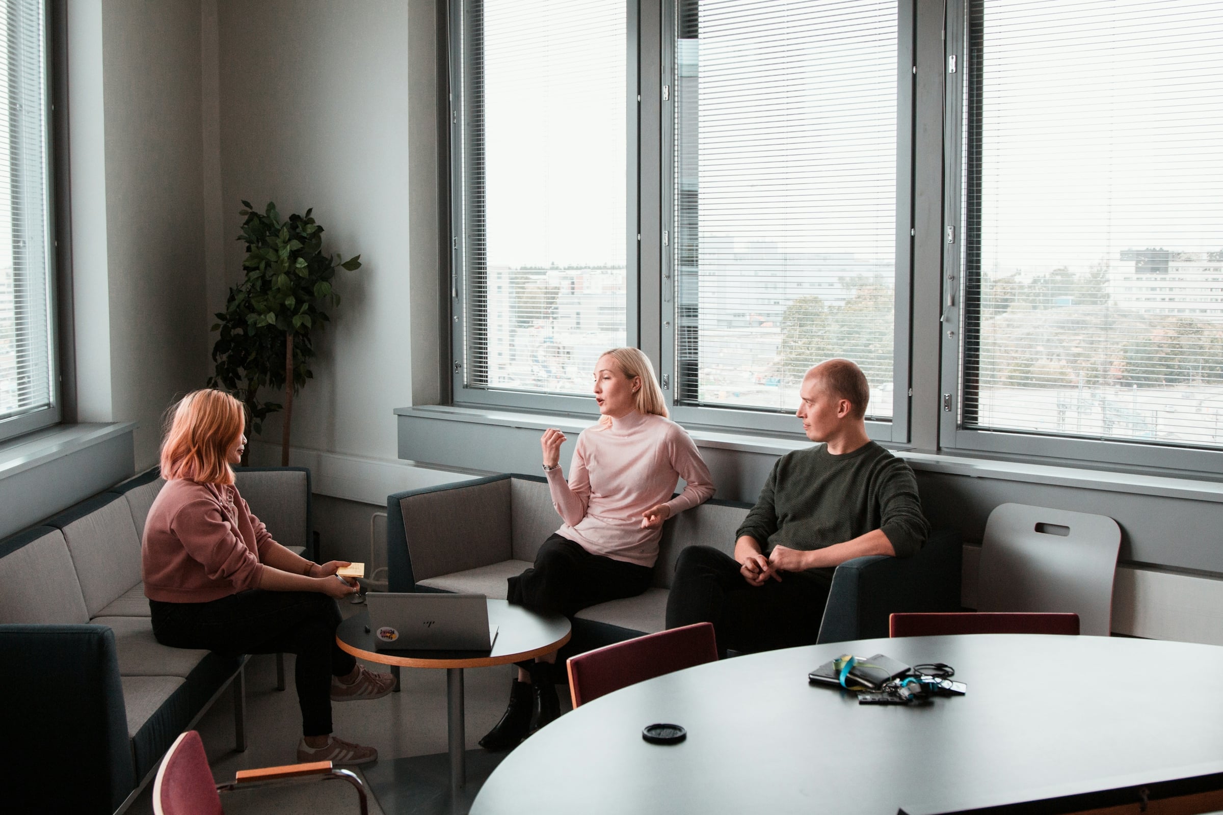 Two people talking across a low table in a bright office lounge with floor-to-ceiling windows