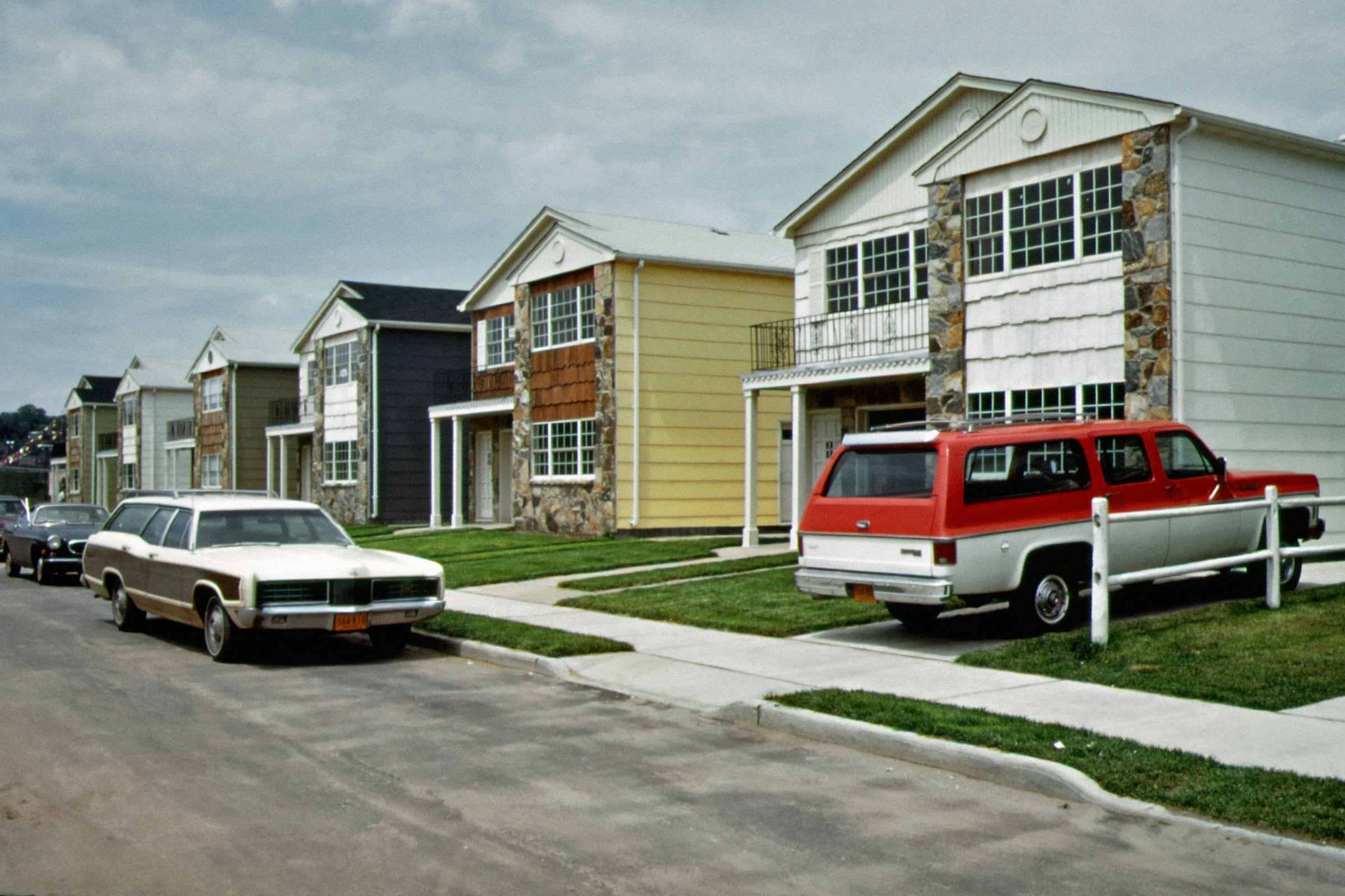 A row of attached two-story townhomes with cars parked along the street out front