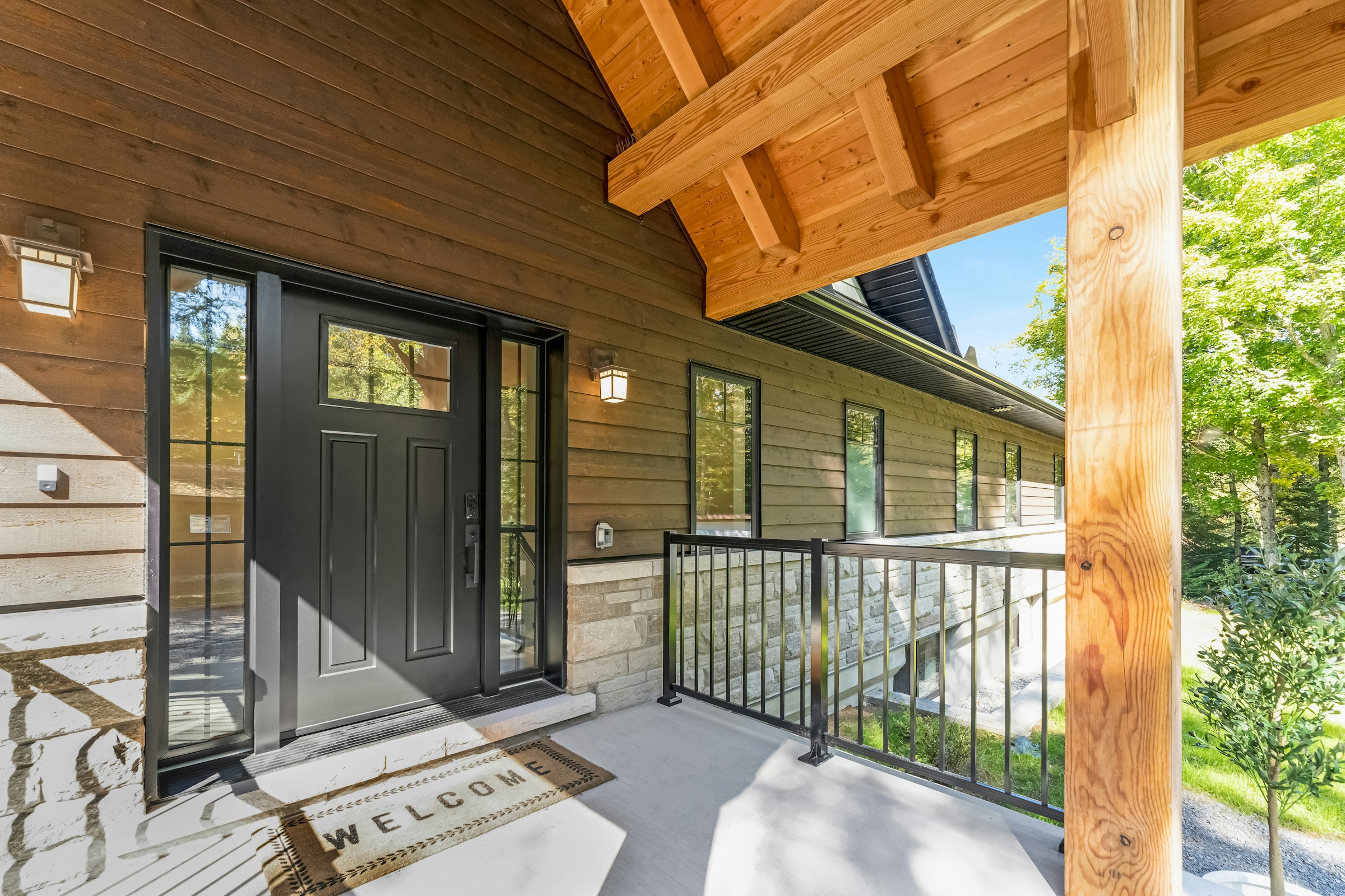 A black front door with a welcome mat on a wooden porch