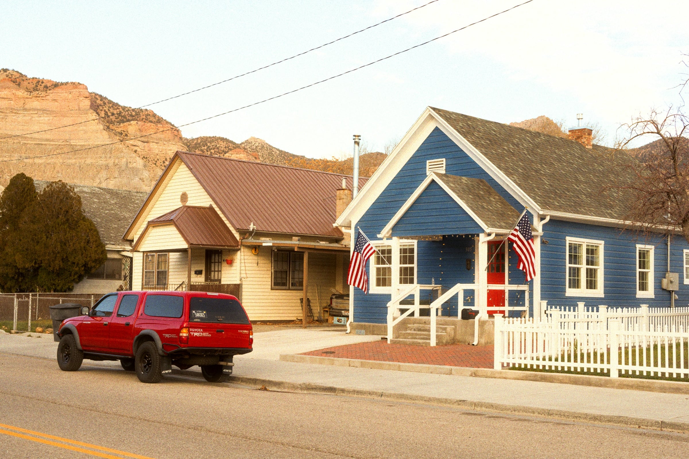 A blue timber craftsman house with a covered porch, an American flag and a red car parked outside
