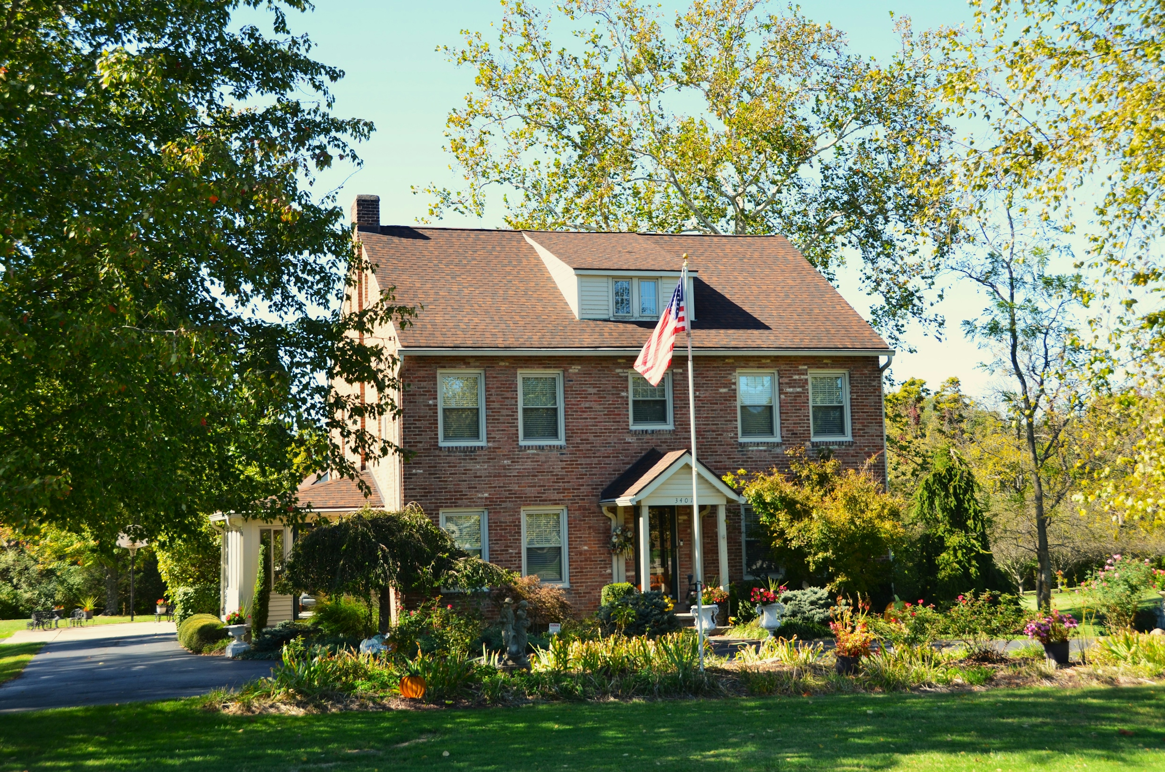 A two-storey brick colonial house with an American flag by the door and autumn leaves on the trees.
